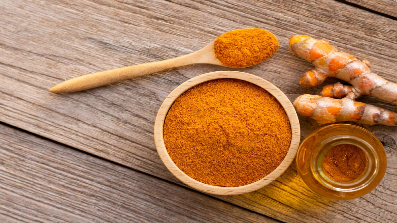Turmeric rhizomes and curcumin extract powder in a wooden bowl